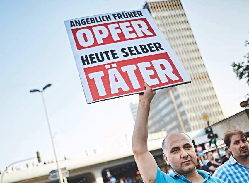 Ein Mann hält ein Plakat hoch, auf dem steht: »Angeblich früher Opfer, heute selber Täter« 